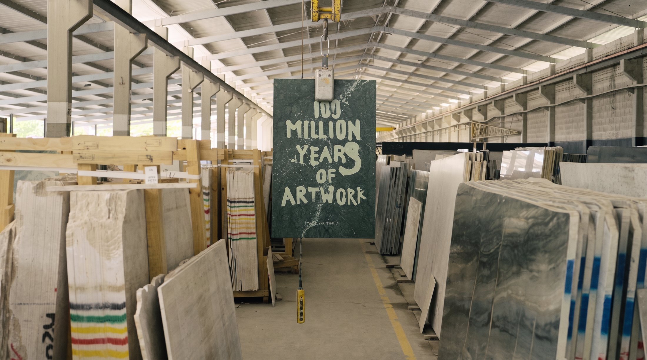 Bodega de placas de mármol con la obra Take Your F*king Time suspendida en el centro del pasillo